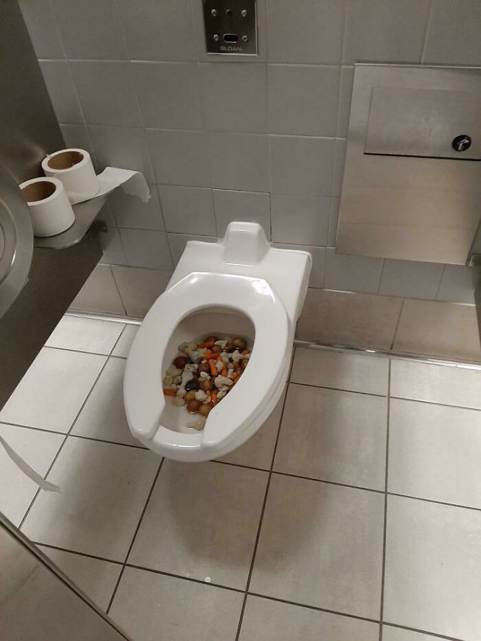 Airports scene: a toilet bowl filled with various types of nuts and snacks, showing a chaotic and unsanitary incident.