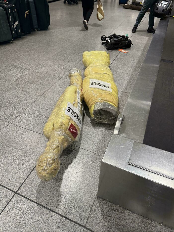 Two oddly shaped, fragile packages wrapped in plastic on an airport floor, among the chaotic airport luggage.