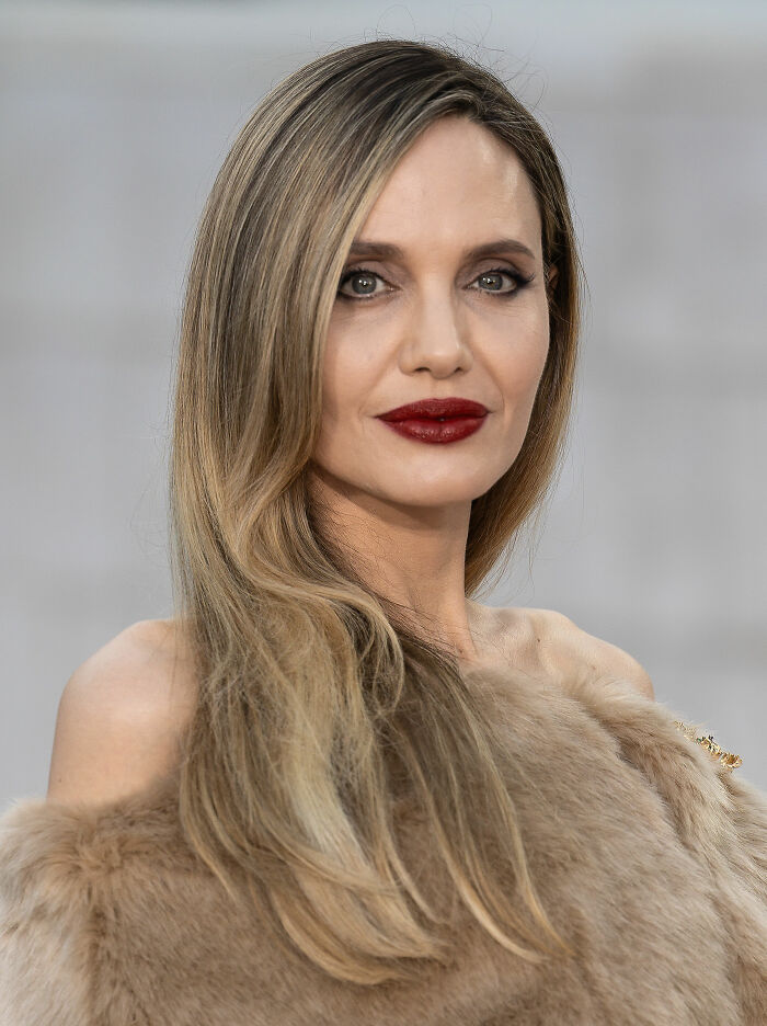 Close-up portrait of Angelina Jolie with long hair and red lipstick in a fur garment