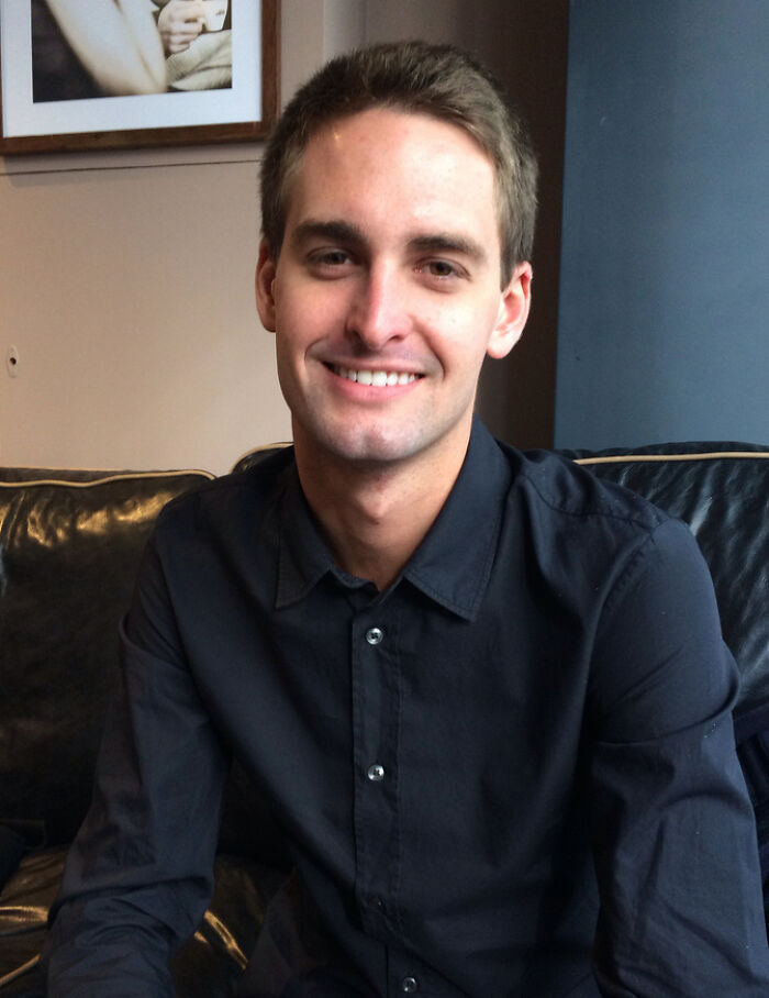 Portrait of Evan Spiegel smiling seated on a couch wearing a black shirt