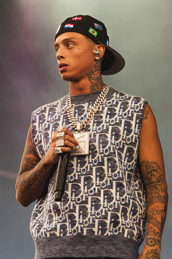 Central Cee performing on stage wearing a patterned sleeveless top and a cap with flags