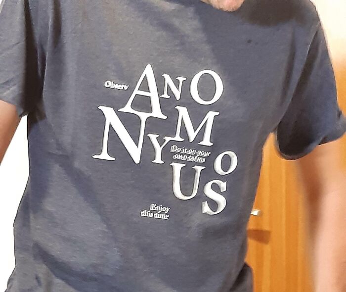 Clothing design: A person wearing a gray t-shirt with the word ANONYMOUS misspelled across the chest.