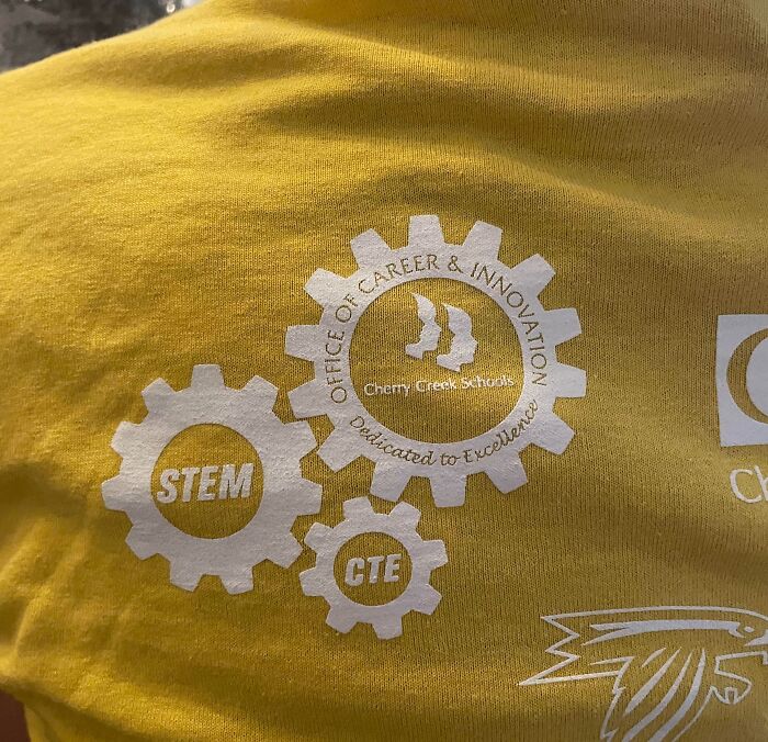 Clothing design: A close-up of a yellow t-shirt with three gear logos, displaying STEM, CTE, and Office of Career & Innovation.