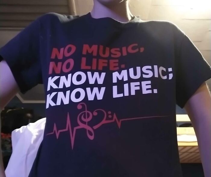 A person wearing a black T-shirt with the text NO MUSIC, NO LIFE. KNOW MUSIC; KNOW LIFE. written in red and white, showing bad clothing designs.