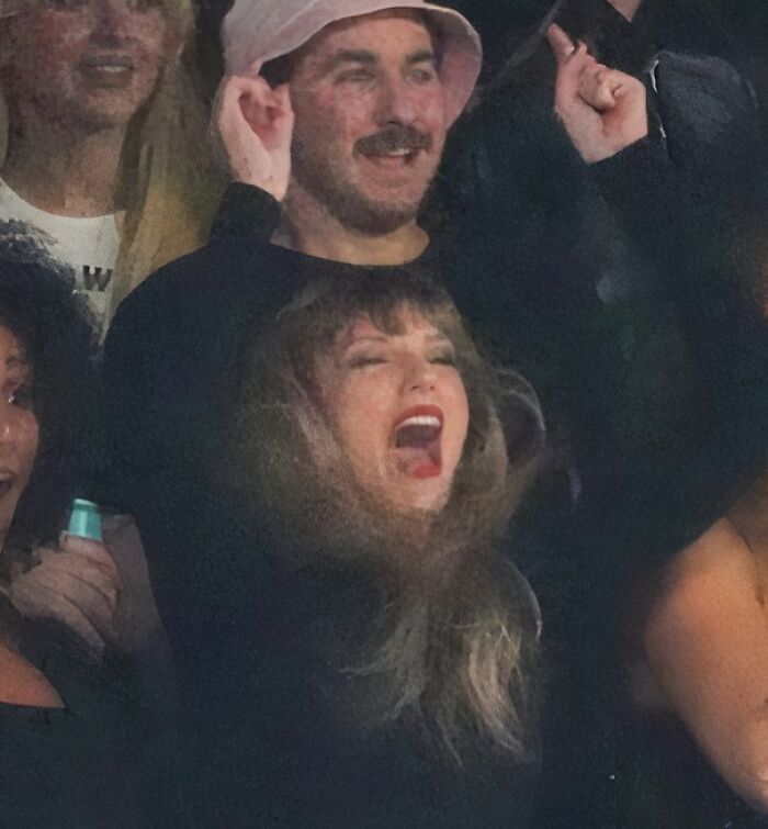 A woman wearing a black long-sleeved shirt with a large print of Taylor Swift's face screaming, a bad clothing design.
