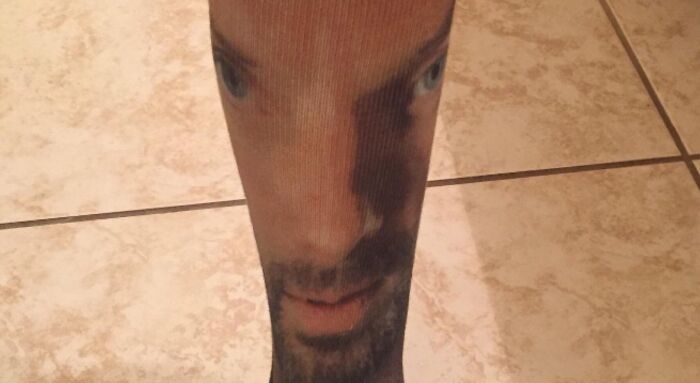 A sock with a man's face printed on it, stretched and distorted on a leg, showing bad clothing designs.