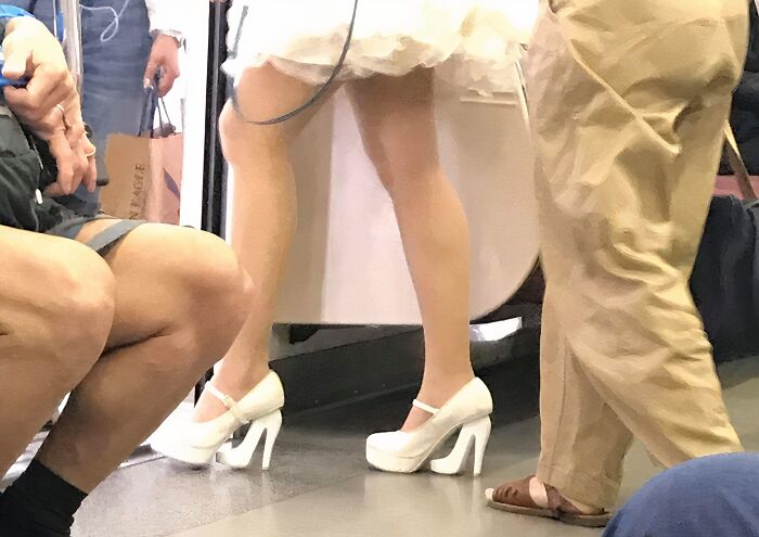 Woman in a white dress and unusual white high heels on a subway, showcasing bad clothing designs.