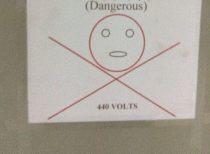 A sign at an airport warning of 440 VOLTS with a skull-like face crossed out, showing airport dangers.