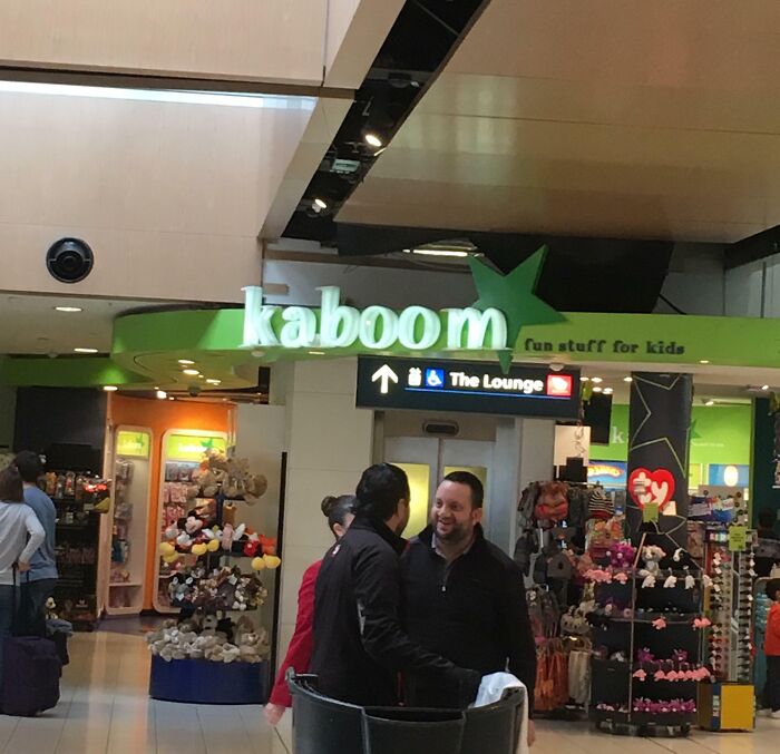 A Kaboom store sign at an airport, featuring fun stuff for kids, amidst the chaotic airport environment.