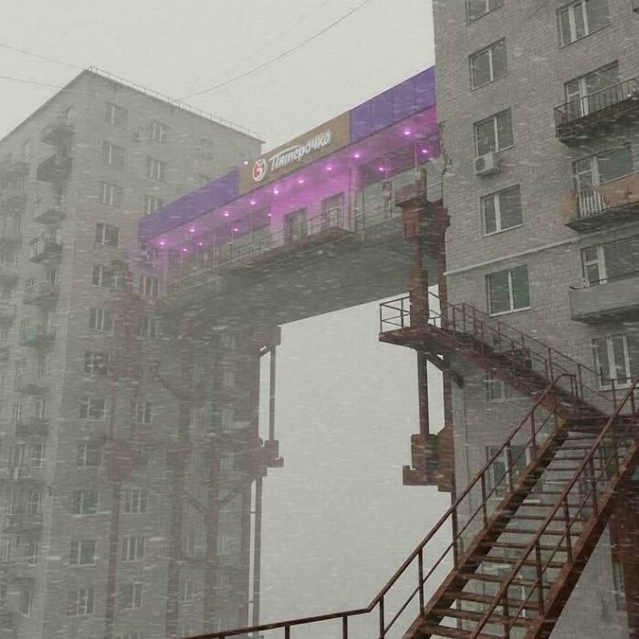 Snowstorm hitting buildings connected by a skybridge with purple lights urban hell