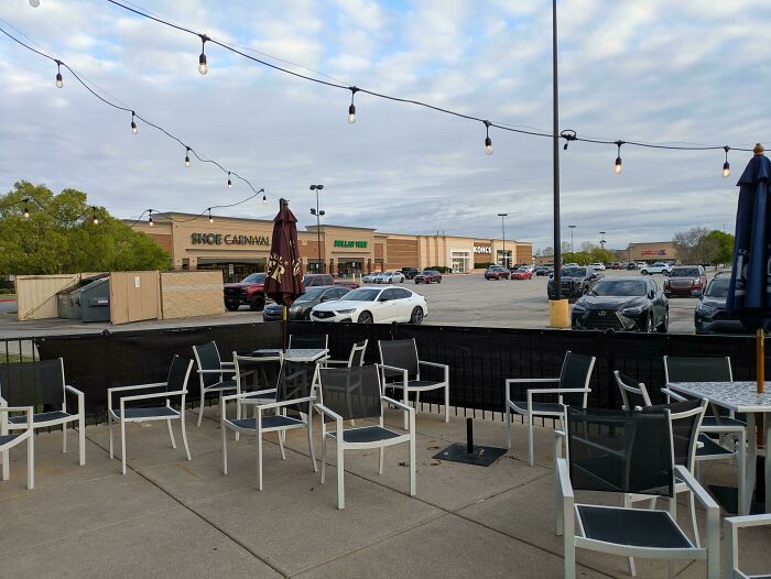 Empty suburban shopping center patio with parked cars and stores
