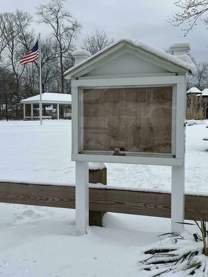 Empty community bulletin board covered in snow with American flag in background