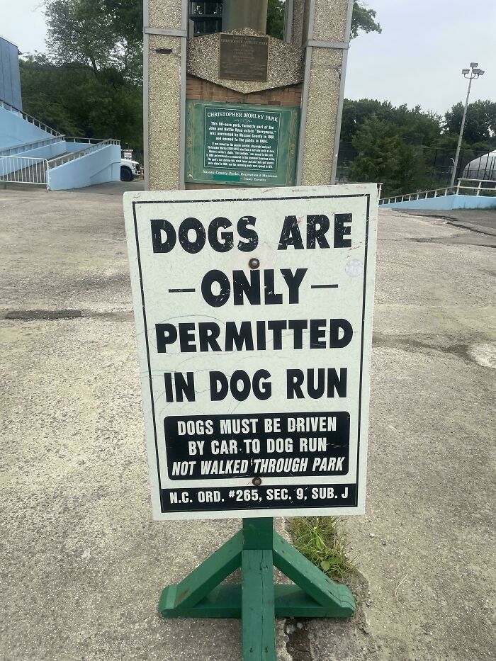 Sign stating dogs must be driven by car to dog run, illustrating suburban hell park rules