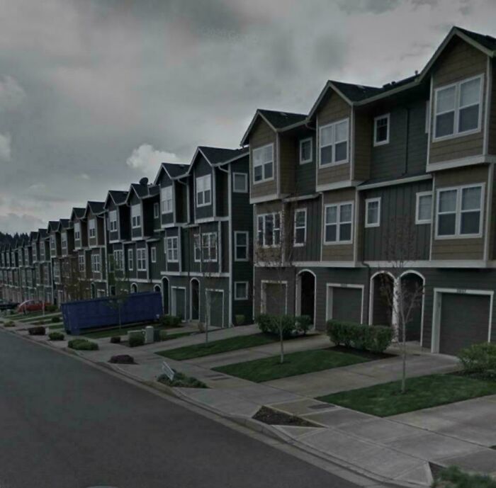 Row of identical dark townhouses under gloomy sky in suburban hell neighborhood