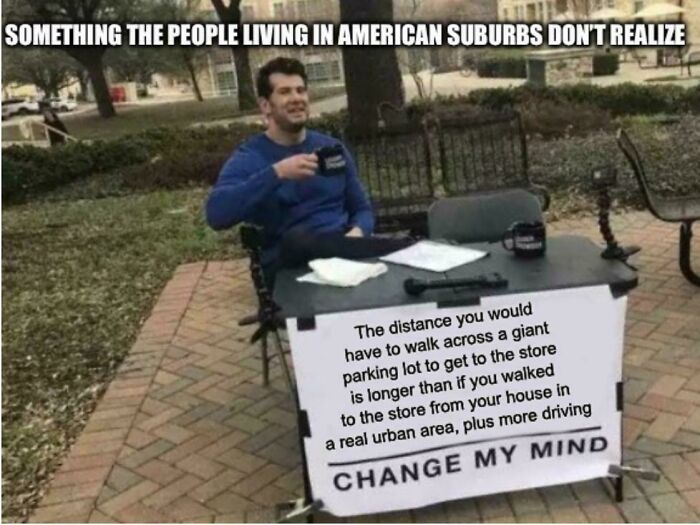 Man at table with sign about long suburban parking lot walks versus urban stores