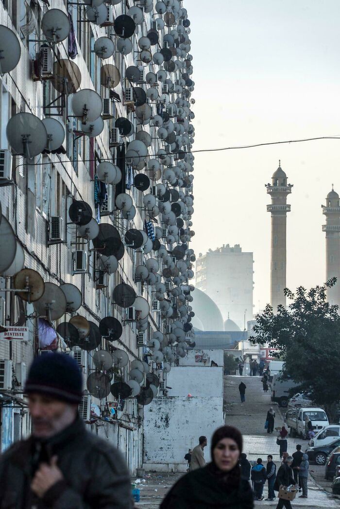 Apartment building facade covered with many satellite dishes in urban area