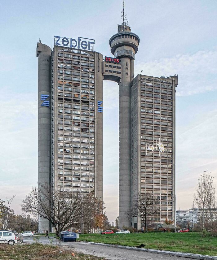Tall brutalist urban building with zepter sign and connecting tower at top