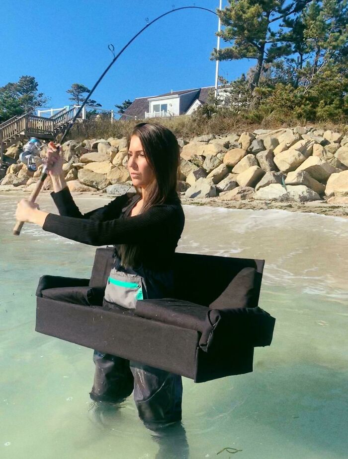 Woman fishing in the ocean while wearing a small black couch around her waist, a quirky take on seating.