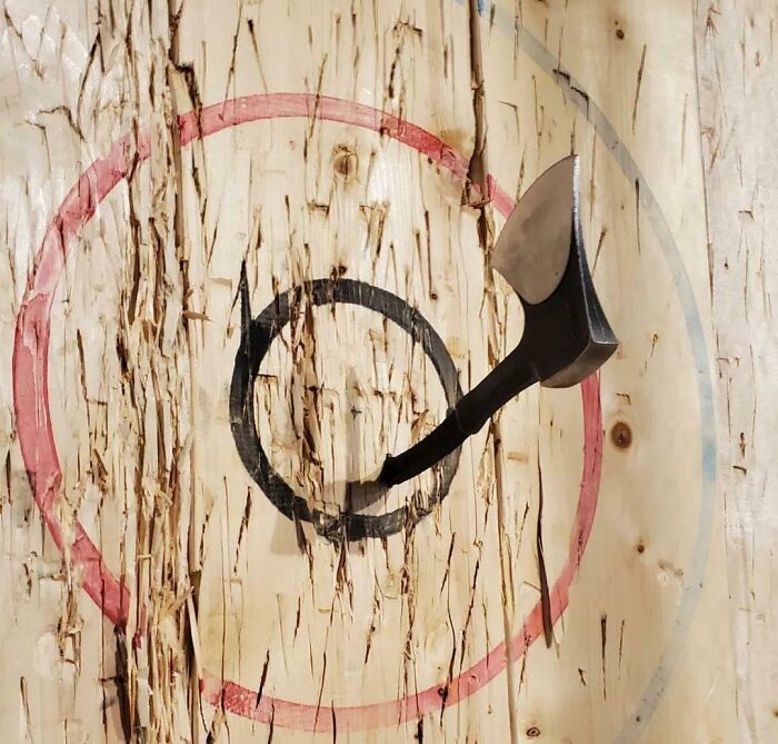 Axe stuck crookedly in the center of a wooden axe throwing target fail