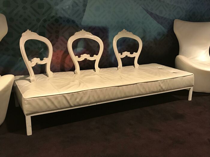 A unique white bench with three ornate chair backs attached, resembling couches for an interior designer.