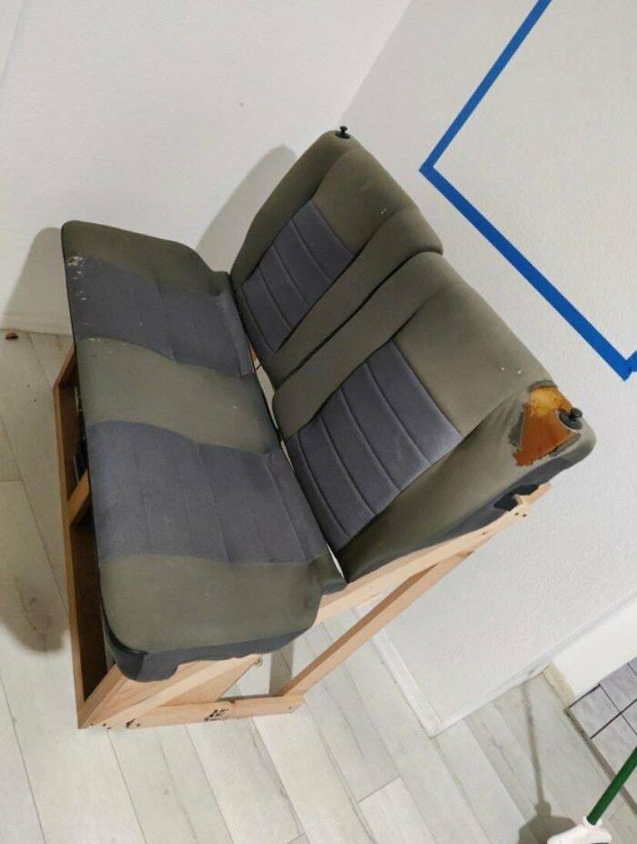 Two car seats forming a couch on a wooden frame against a white wall with blue marks, innovative interior designer concept.