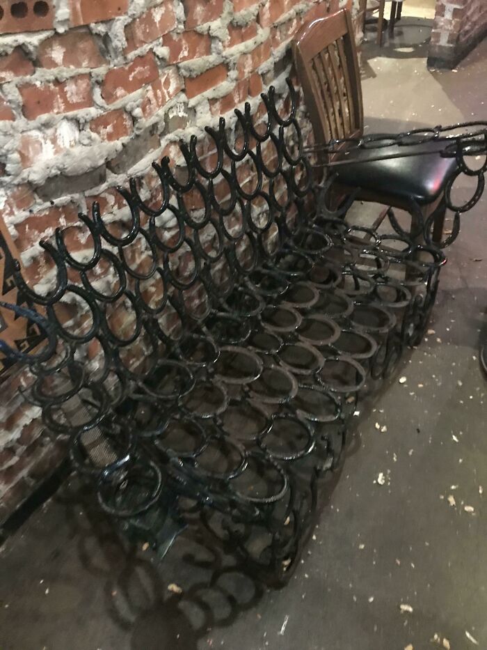 Rustic couches made from welded horseshoes against a brick wall, showcasing unique interior designer creations.