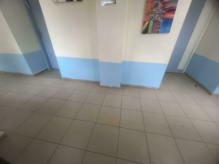 A school hallway with light blue and white walls and tiled floors, representing a typical school environment where teachers interact with students.