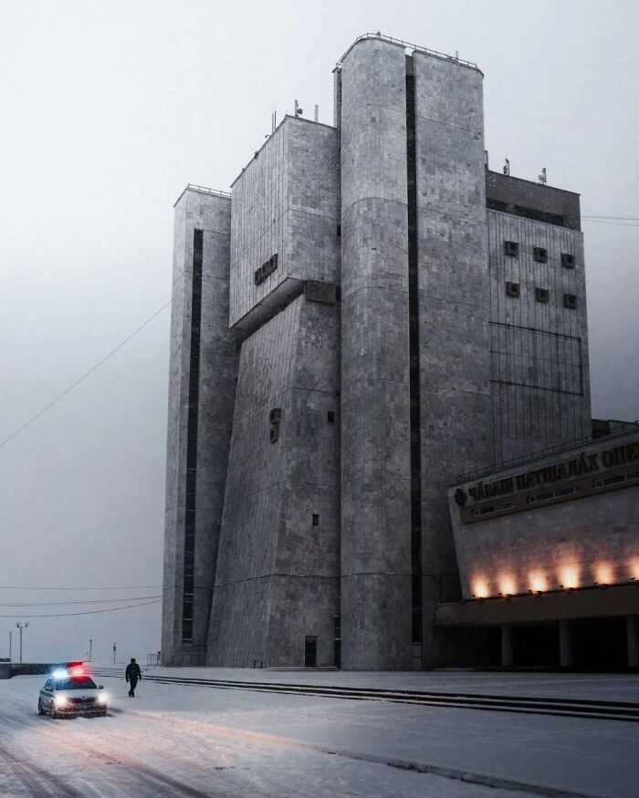 Bleak urban hell brutalist building in snow with police car and lone figure