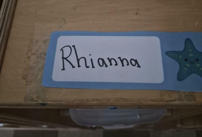 A desk name tag for a student, Rhianna, on a wooden desk. Teachers can be toxic and annoying.