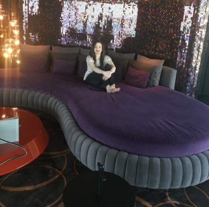 Woman sitting on a large, purple, wavy couch, showcasing unique interior design and comfort.