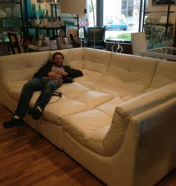 A man lounging comfortably on an oversized white leather couch, a luxurious option for any interior designer looking for large couches.