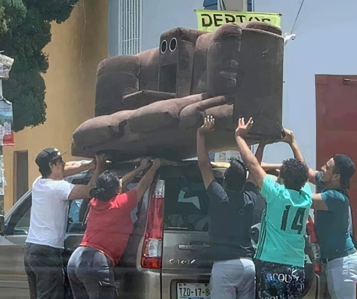 Several people struggling to carry a large brown couch, highlighting the effort involved with unique couches.