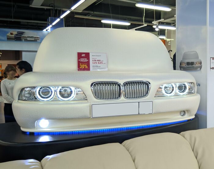 A unique white car-shaped couch with glowing headlights, perfect for an interior designer looking for creative couches.