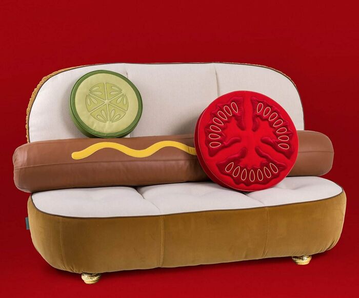 A fun hot dog-shaped couch with pickle and tomato cushions, a whimsical choice for an interior designer.