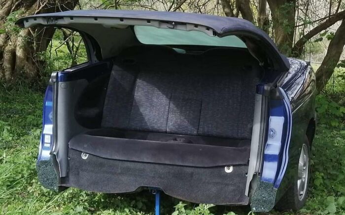 A car interior repurposed as a couch, with a blue fabric backrest and trunk open, a quirky choice for interior designers couches.