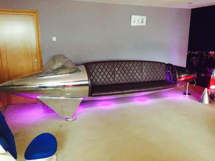 A unique spaceship-shaped couch with brown leather seating and purple under-lighting, an interior designer's dream.