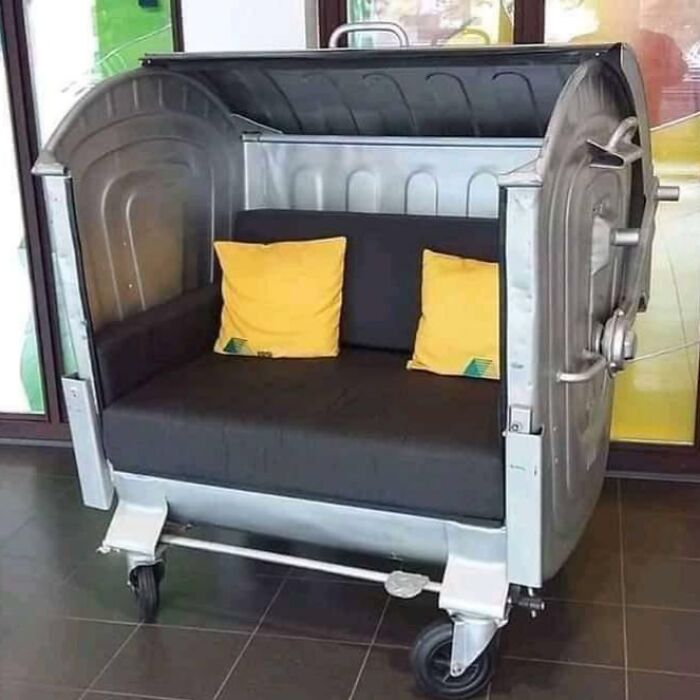 A repurposed metal dumpster transformed into a modern couch with yellow pillows, an avant-garde interior design concept.