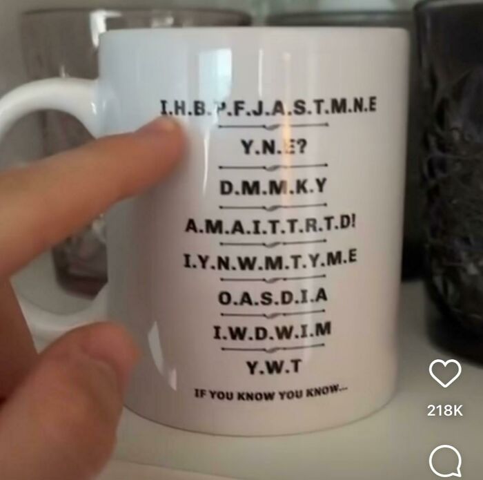 A white mug with a brain puzzle written in acronyms, challenging the viewer to decipher the message.