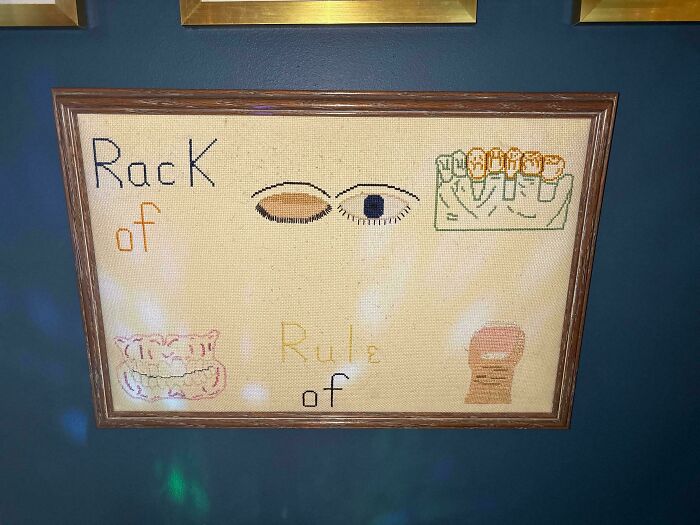 A framed cross-stitch brain puzzle with the words Rack of, Rule of, eyes, and teeth.