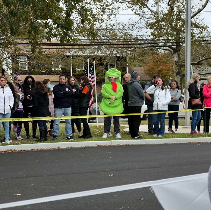 Crowd lined up with person in green dinosaur costume at event fail