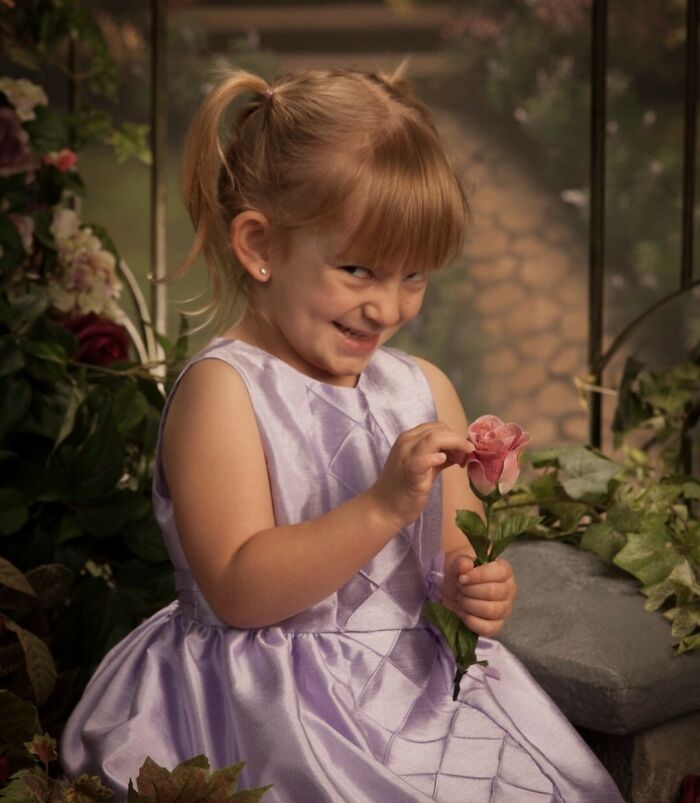 Funny toddler smirking mischievously holding a flower in purple dress