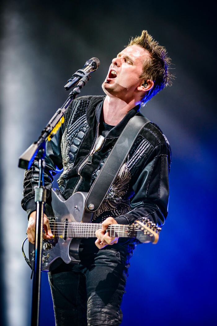 Matt Bellamy performing live on stage playing electric guitar and singing into a microphone