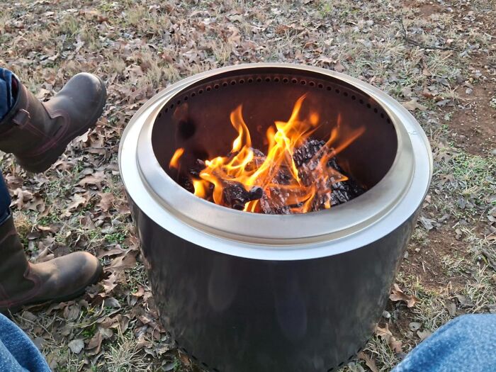 Outdoor metal fire pit with flames burning and person sitting nearby