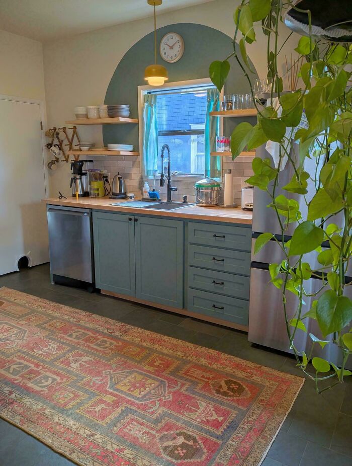 A kitchen with teal cabinets, a patterned rug, and creative home decor projects enhancing the window area.