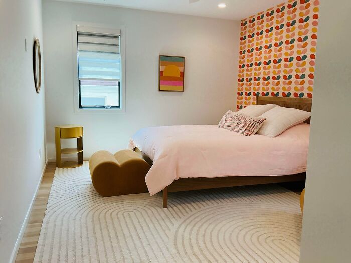A bedroom home decor project with a pink bed against a vibrant, patterned wallpaper accent wall, complemented by a unique yellow side table and a soft rug, showcasing a cheerful and modern design.