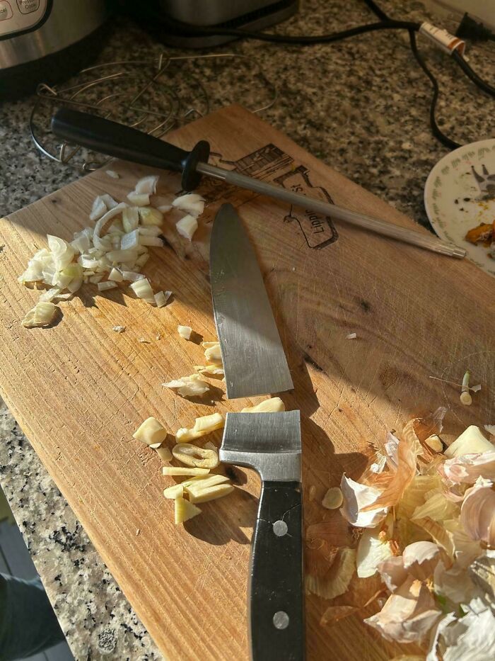 Mildly interesting picture of a broken knife blade on a cutting board with chopped onions and garlic.