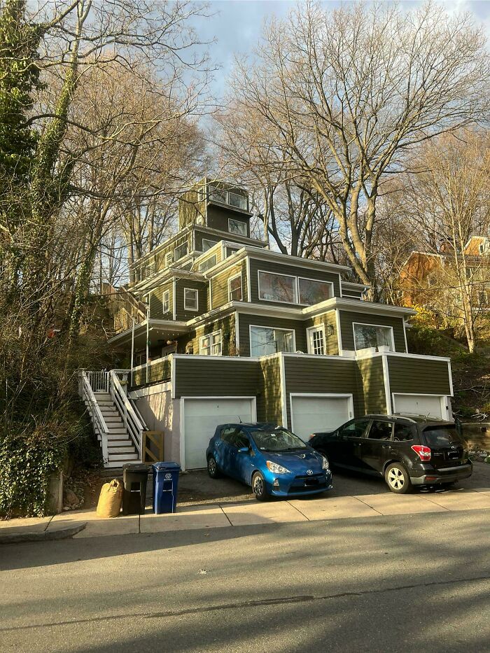 Mildly interesting picture of a unique, tiered green house nestled on a hill with bare trees and cars.