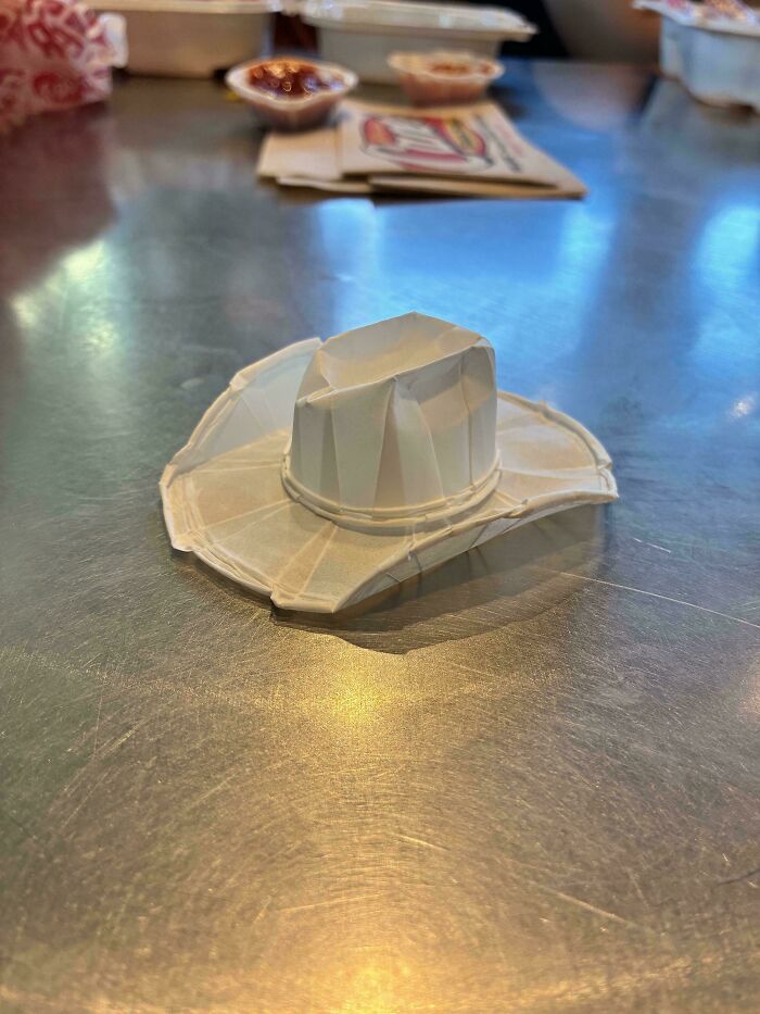 A mildly interesting picture of a miniature paper cowboy hat on a metallic surface, with blurred background elements.