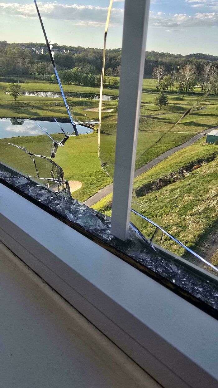 A mildly interesting picture of a broken window overlooking a golf course with ponds and trees under a bright sky.