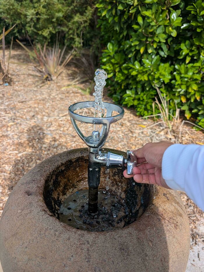 Mildly interesting pictures: A hand turning on a stone outdoor water fountain with water flowing upwards.